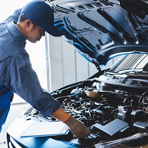 A mechanic checks under a car hood for any auto services needed