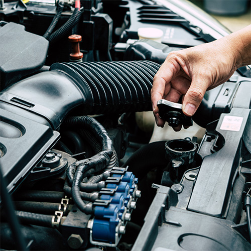 A car part is held above an open car hood before cooling system services